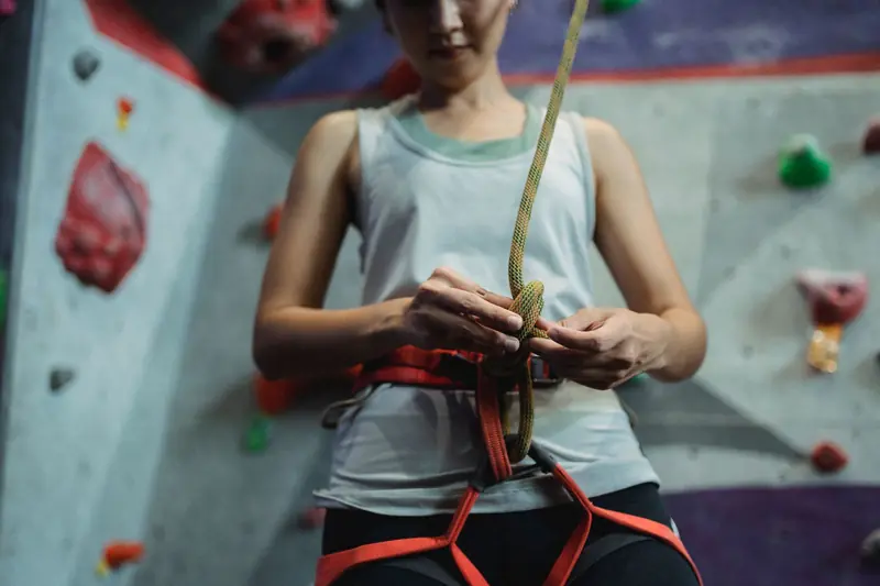 From below crop slim female climber in sportswear fastening rope on safety belt before climbing in modern bouldering center