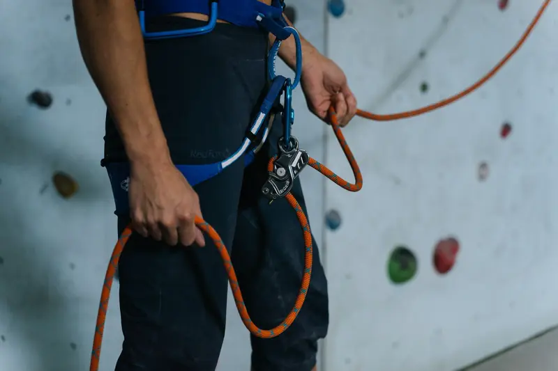 Close-up of climber securing harness with carabiner and rope on indoor wall