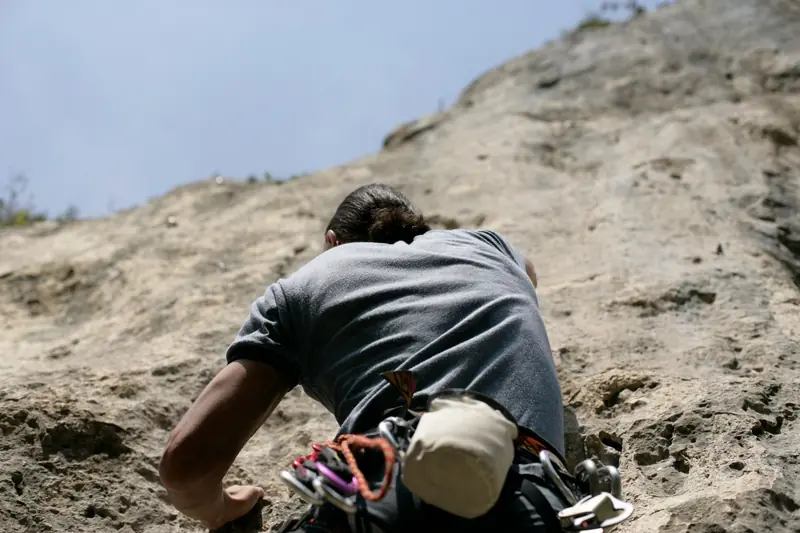 A determined climber scaling a rugged cliff face on a clear day, capturing the essence of adventure