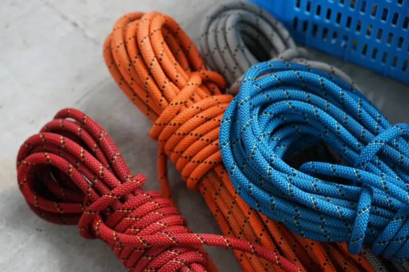 Vibrant red, orange, and blue climbing ropes coiled on concrete surface