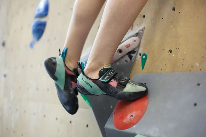 A close-up of a climber's feet wearing climbing shoes on an indoor climbing wall