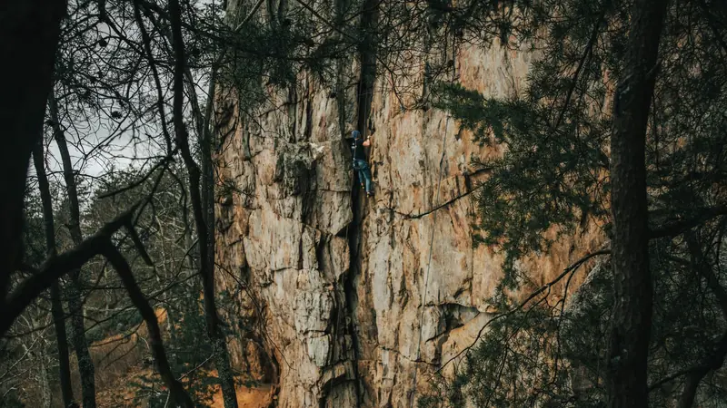 A climber ascends a rocky cliff surrounded by trees in Gastonia, NC