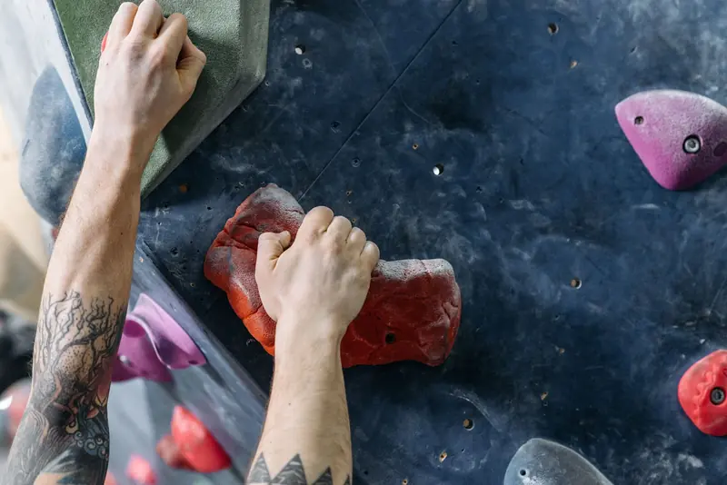 A focused shot of a climber's tattooed arms gripping brightly colored holds on an indoor climbing wall