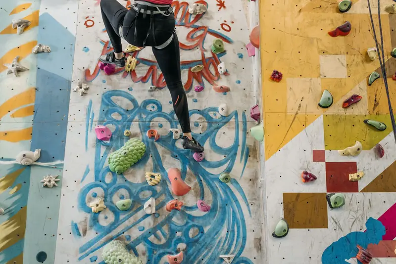 A climber scales a colorful indoor rock climbing wall with various holds