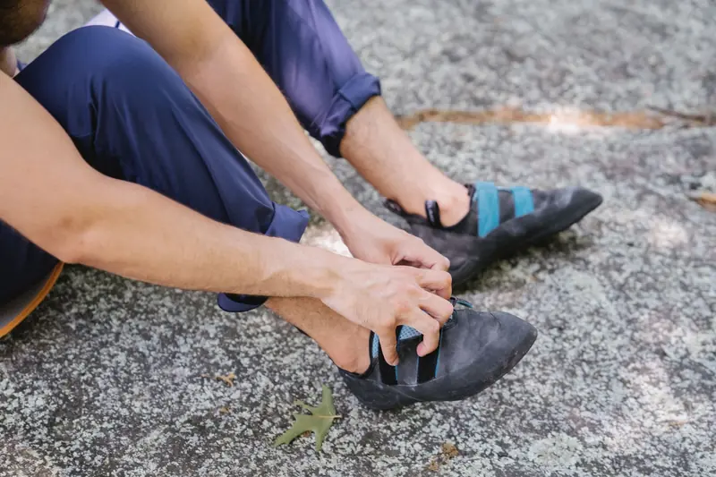 Man sitting on a rocky surface outdoors adjusting climbing shoes, preparing for a climbing session