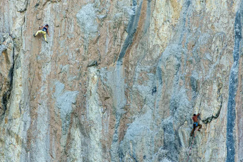 Two rock climbers tackle a steep, textured cliff face, showcasing their skill and determination