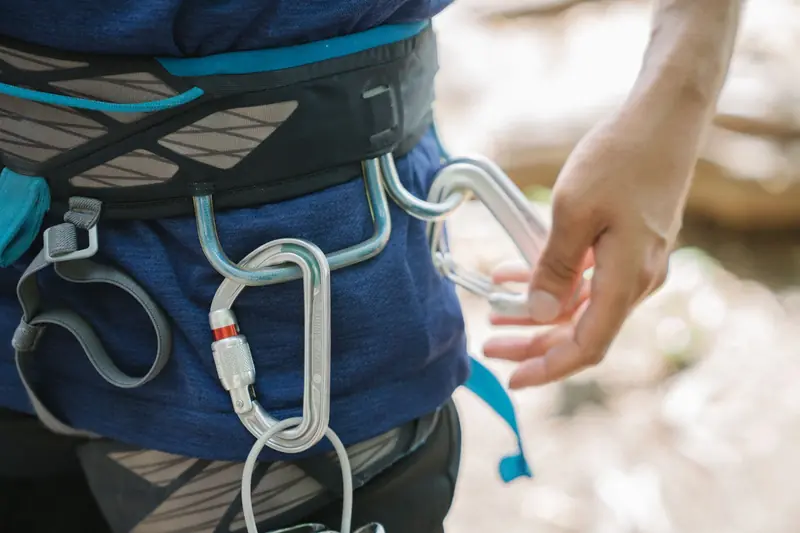 Detailed view of a person's climbing harness with carabiners and hand adjusting the setup