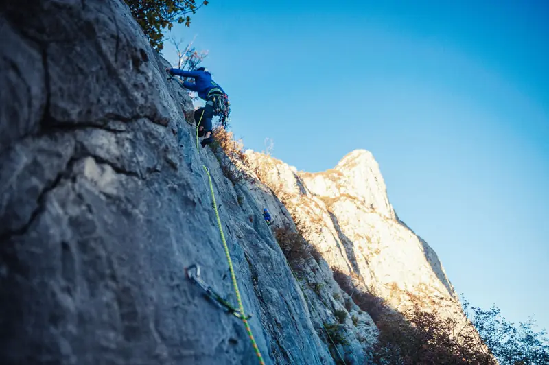 Adventurous rock climber ascending steep mountain face with safety gear in sunlight