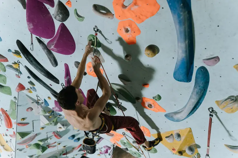 Man climbing an indoor rock wall with colorful holds, showcasing strength and focus