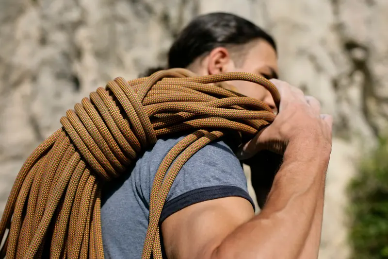 Close-up of a man carrying climbing rope, ready to ascent an outdoor rock face