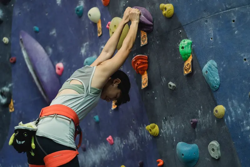 From below of focused female climber in activewear standing near climbing wall and stretching before training in gym