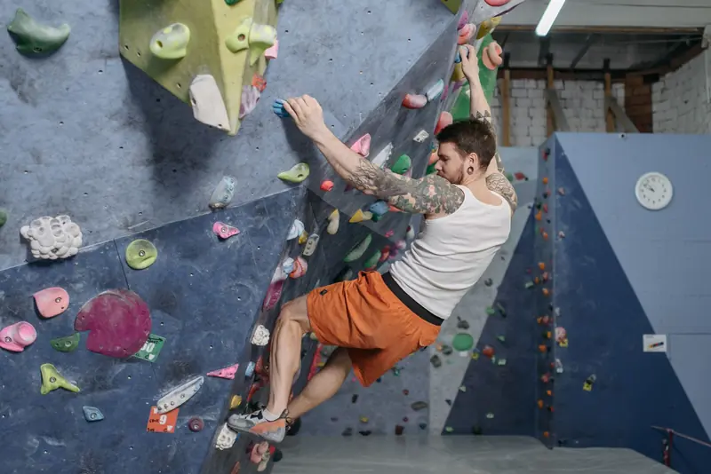 Adult male rock climber on indoor bouldering wall, showcasing athletic training and focus