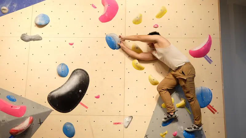 Adult male climber scaling an indoor bouldering wall with colorful holds