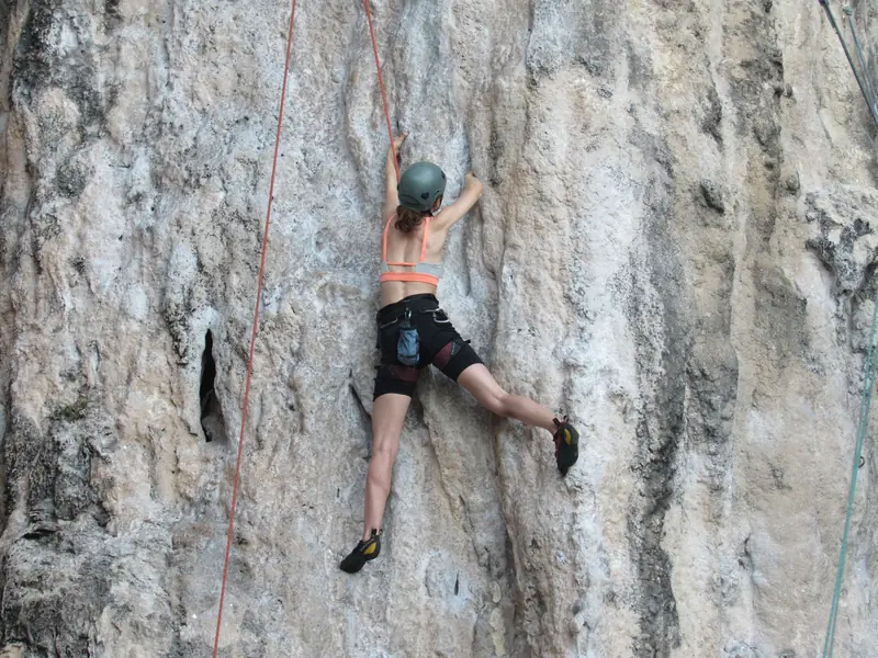 Woman climbing a limestone cliff with ropes. Outdoor sport showcasing strength and adventure
