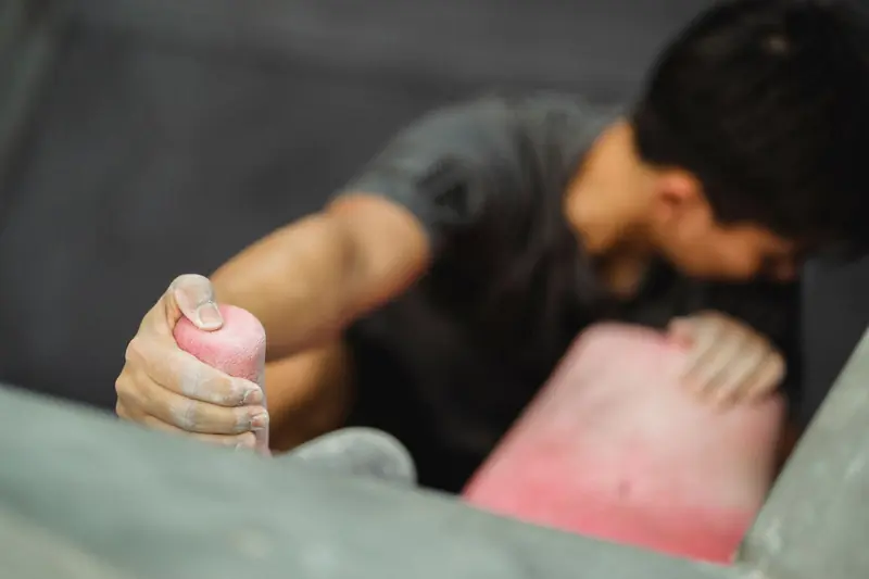 From above of crop anonymous male climber in sportswear practicing rock climbing on climbing wall while looking down in modern gym