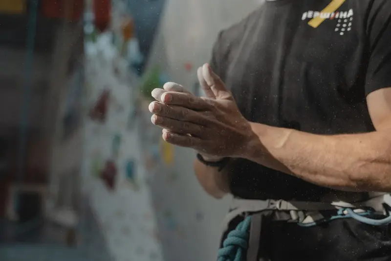 Close-up image of a climber dusting hands with chalk, preparing for indoor climbing on a colorful wall